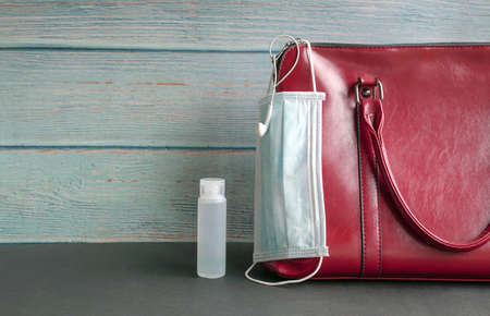 Face mask hanging on woman handbag with hand sanitizer by the side. Health and safety while on the move concept.の写真素材