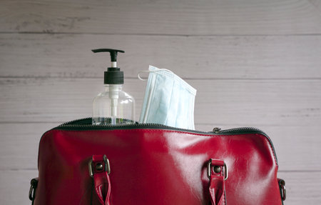 Face mask and hand sanitizer inside woman red handbag. Health and safety from concept.