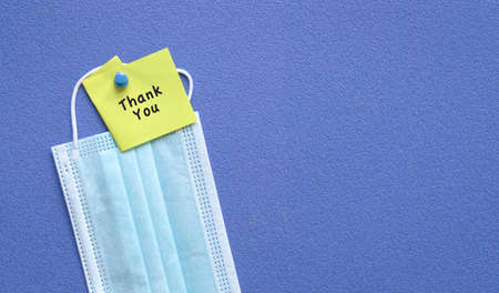 Thank you note on top of medical face mask. Pin on blue board. Copy space.