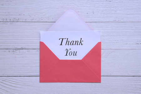 Thank you card inside a red envelope. On white wood background.