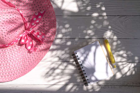Notepad and pen with pink summer hat. Top view with light and shadow.の写真素材