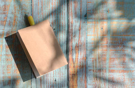 Notepad with yellow pen on top of rustic wood table with shadow of palm leaves. Copy space.の写真素材