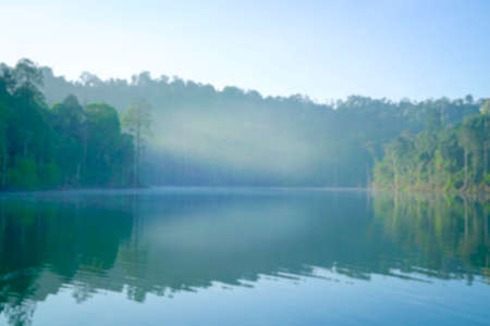 Defocused bokeh background of forest and lake with morning fog. Nature backdrop concept.の写真素材