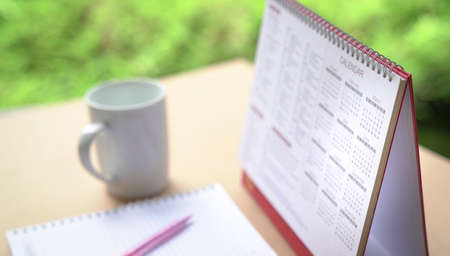 Calendar on table with cup of coffee and notebbok, Selective focus. Green nature at the background.の写真素材