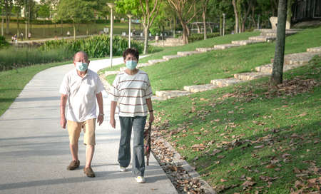 Senior Asian couple wearing face mask taking a walk in a green park. Healthy lifestyle during...