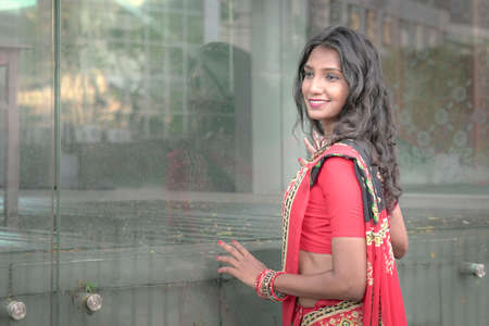 Side view of a beautiful and smiling Indian woman wearing red saree. Outdoor setting.の写真素材