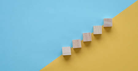 Wood block stacking as step stair. On blue and yellow background. Business concept for growth success process.の写真素材