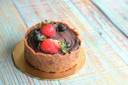 Chocolate tart with strawberries and blueberries topping. On rustic wood table, copy space.