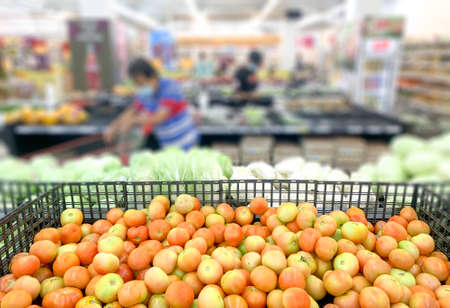 Shopping inside supermarket grocery section, defocused. Selective focus on tomatoes.