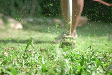 Grass cutting. Man using grass trimmer to mow lawn. Defocused. Machine in motion and grass particles in the air.の写真素材