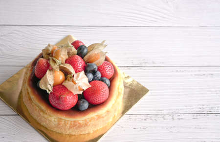 Burnt Cheese Cake decorated with fruit strawberries and blueberries topping. On white wooden table,...