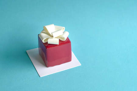 Gatou cake in the form and shape of gift box wrapped with ribbon. On blue background, copy space.