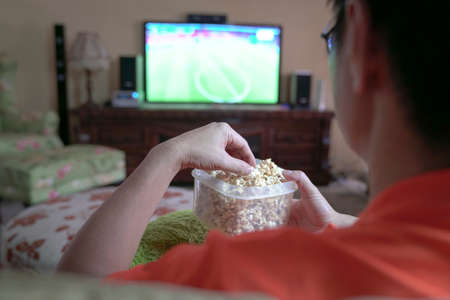Man watching TV sporrts program at home and eating popcorn. Stay home quarantine.
