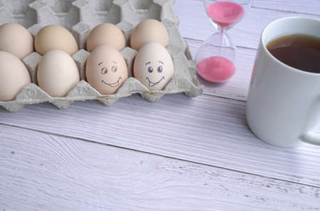 Two eggs painted with smiling face next to a red coffee cup and hourglass sand timer. Copy space.