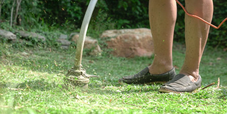 Man mow lawn of garden with electric grass trimmer machine.