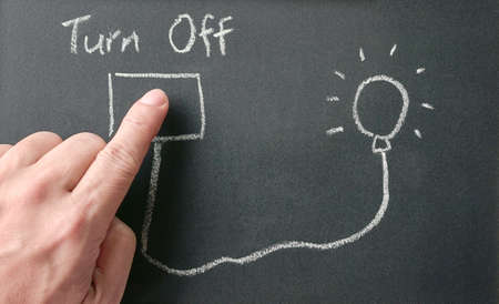 Man's finger on drawing of power outlet that connects power to light bulb on blackboard with words, turn off. Save energy concept.の写真素材