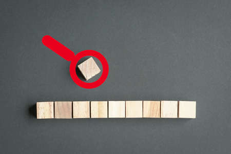 Wood cubes on a row and a single cube outside the row with magnifying glass icon on top. Leadership or stand out concept.の写真素材