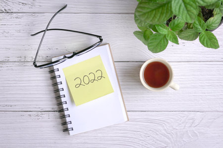 2022 on yellow paper on top of notepad, with coffee and green plant on wood tabletop. Top view.の写真素材