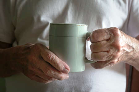 Senior man holding a cup of hot drink. Close up view of his wrinkled hands.の写真素材