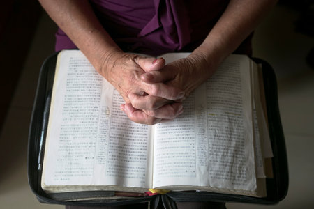 Close up view of senior woman hands on open bible, folded in prayer. Top view.の写真素材