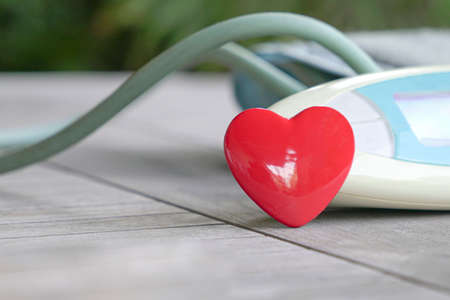 Red color heart shape next to digital blood pressure gauge. Health and medical concept.の写真素材
