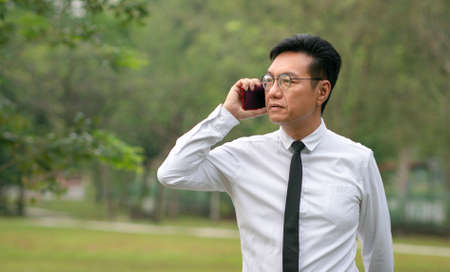 Asian mature businessman having a phone call outdoor. Copy space.の写真素材