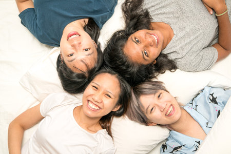 Group of young multi-ethnic Asian women lying in bed, happy and smiling, top view. Friends sleep over party concept.の写真素材