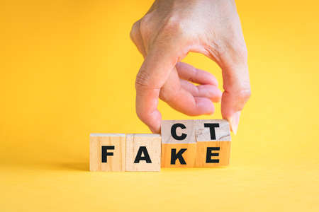 Hand flipping wooden cubes block, from fact to fake wording. On yellow background.の写真素材