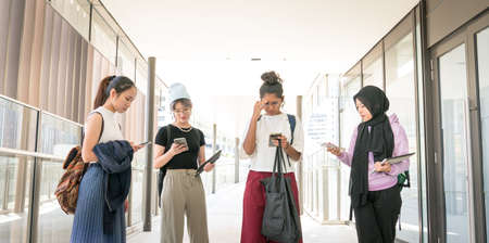 Group of multi-racial college female students looking down at their smartphone in the campus hall.の写真素材