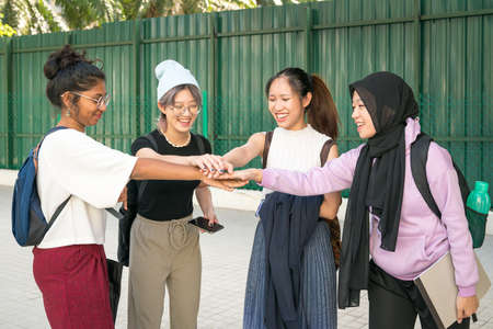 Group of happy young women students putting and stacking their hands together. Unity and teamwork...