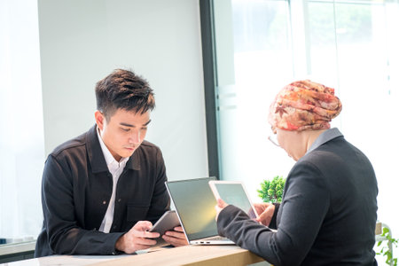 Two Asian business people working together, looking at tablets in office.の写真素材