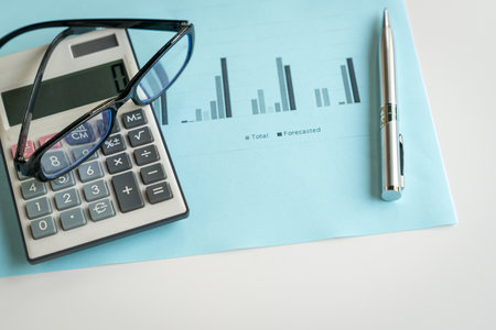 Eyeglasses, calculator and pen on top of report with charts. Financial analysis and market trends...