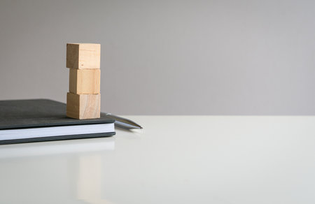 Three blank wooden block cubes stacked on top of a notepad with pen. Free text and template for business concept.の写真素材