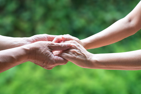 Two people holding hand together, with green nature background. Helping hand or emotional support...