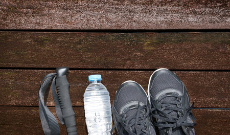 Hiking stick, water bottle and sport shoes on wooden planks. Hiking or exercise concept.の写真素材