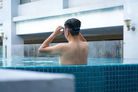 Back view of man in the pool, relaxing and adjusting his goggles by the side. Vacation or travel...