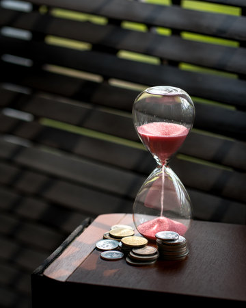 Sand running or flowing down of an hourglass with coins next to it. Copy space. Time is money concept.の写真素材