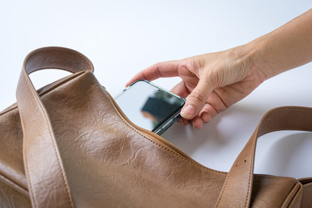 Woman put inside phone into brown leather handbag. Top view.の写真素材