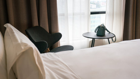 Hotel room with bed covered with white blanket, chair and table.の写真素材