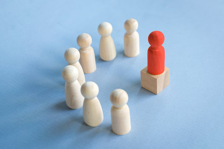 Red toy block standing on podium facing other toy blocks standing in semi circle on desk. Illustrate leadership concept.の写真素材