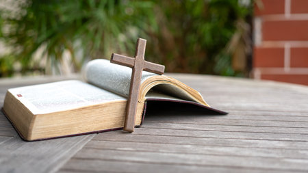 Wooden crucifix cross next to Holy Bible. On top of wood table. Copy space.の写真素材