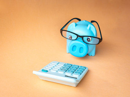 Piggy bank with eyeglasses facing calculator. isolated on orange background, copy space.の写真素材