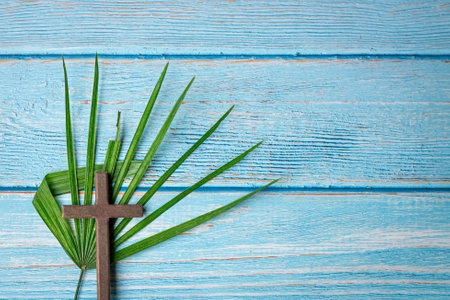 Crucifix cross and palm leaf on rustic wooden table. Copy space. Easter celebration concept.の写真素材
