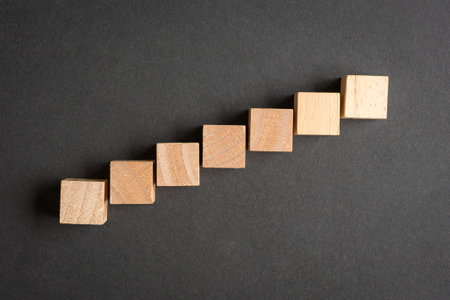Seven blank square wooden blocks in short steps up direction on dark background. Top view.