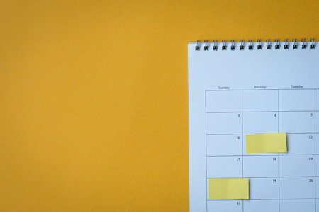 Calendar page with yellow adhesive post it notes. On top of yellow surface, high angle view. Copy space.の写真素材