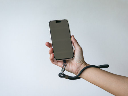 Hand holding phone with a wrist lanyard strap. Isolated on white background.の写真素材
