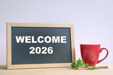 Welcome 2026, on chalkboard next to red coffee cup.