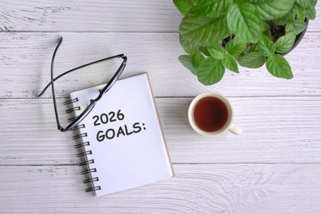 2026 goals on notepad. With eyeglasses, coffee and green plant on white wood table. Top view.