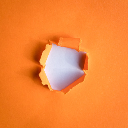 Round hole ripped in orange paper on white background. Copy space.の写真素材