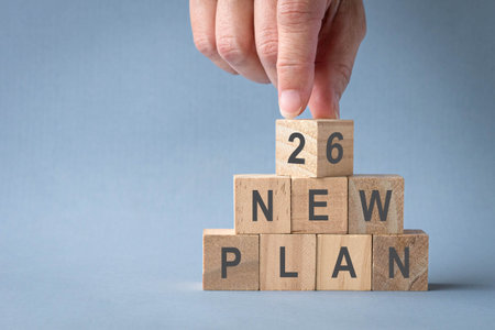 2026 New Plan, words on stacked wooden blocks, isolated on light blue background.